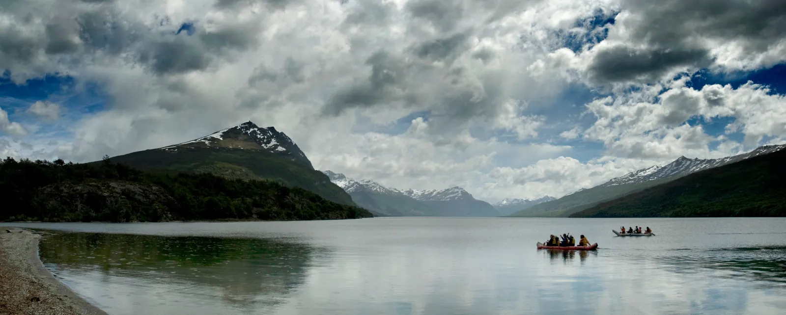Canoes crossing a calm lake below a mountain