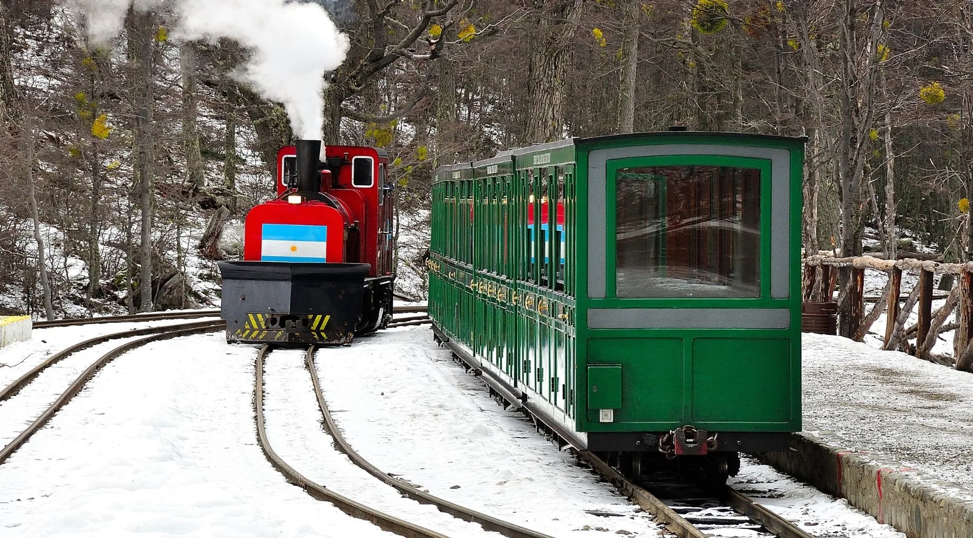 Steam locomotive and a green carriage waiting in the snow